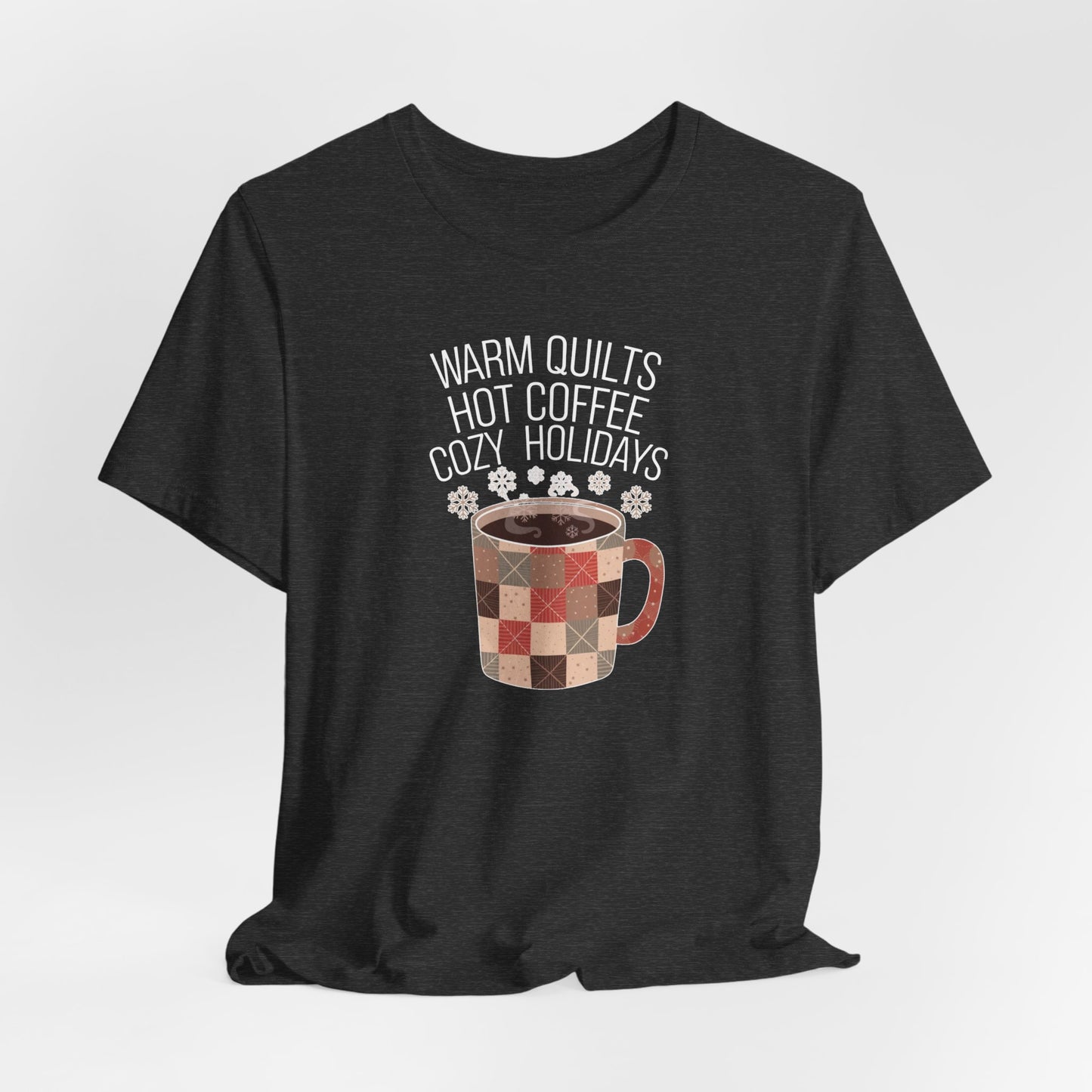 A Dark Grey Heather christmas quilting t-shirt featuring a cozy patchwork quilt-themed coffee mug, surrounded by snowflakes, with the phrase "Warm Quilts, Hot Coffee, Cozy Holidays" above the mug, celebrating the warmth of quilts and coffee during the holiday season.