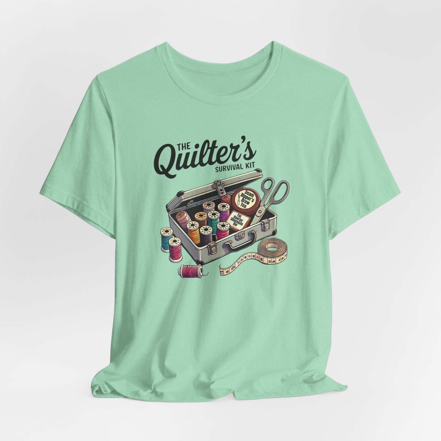 A Heather Mint t-shirt featuring a whimsical illustration of a quilter’s survival kit with colorful thread spools, scissors, and a tape measure, perfect for sewing and quilting enthusiasts.