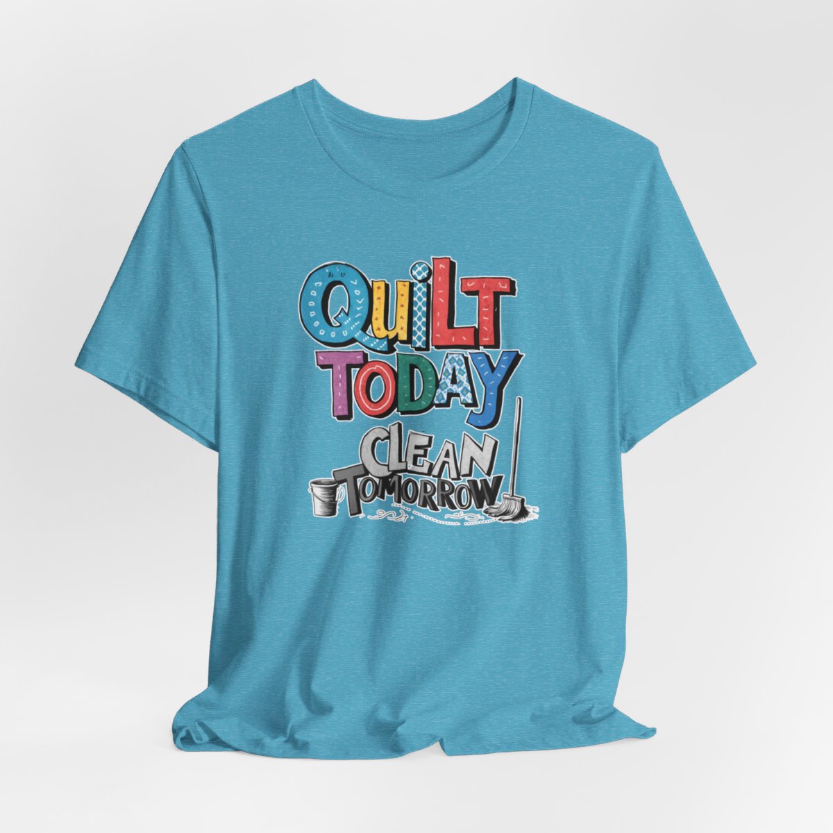A Heather Aqua funny quilting T-Shirt with the phrase Quilt Today, Clean Tomorrow in a bold and cheerful font with a broom off to the side