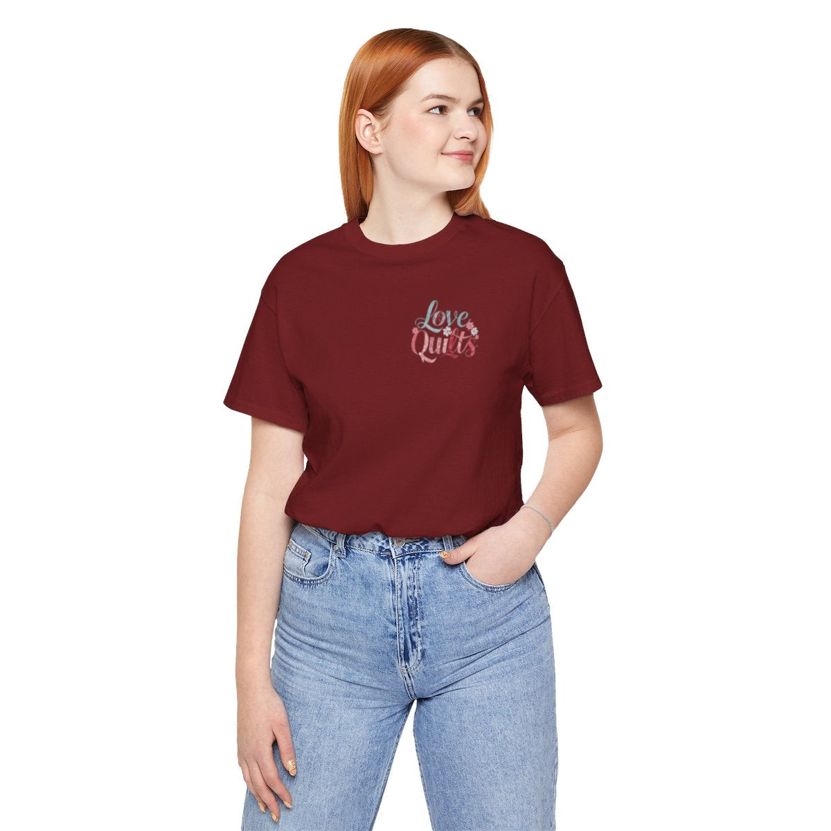 A Cardinal t-shirt spelling out "Love Quilts". The word "Love" is in teal, while "Quilts" features various shades of pink and red. Small flowers in white and pink adorn the letters, creating a floral and quilting-inspired artwork.