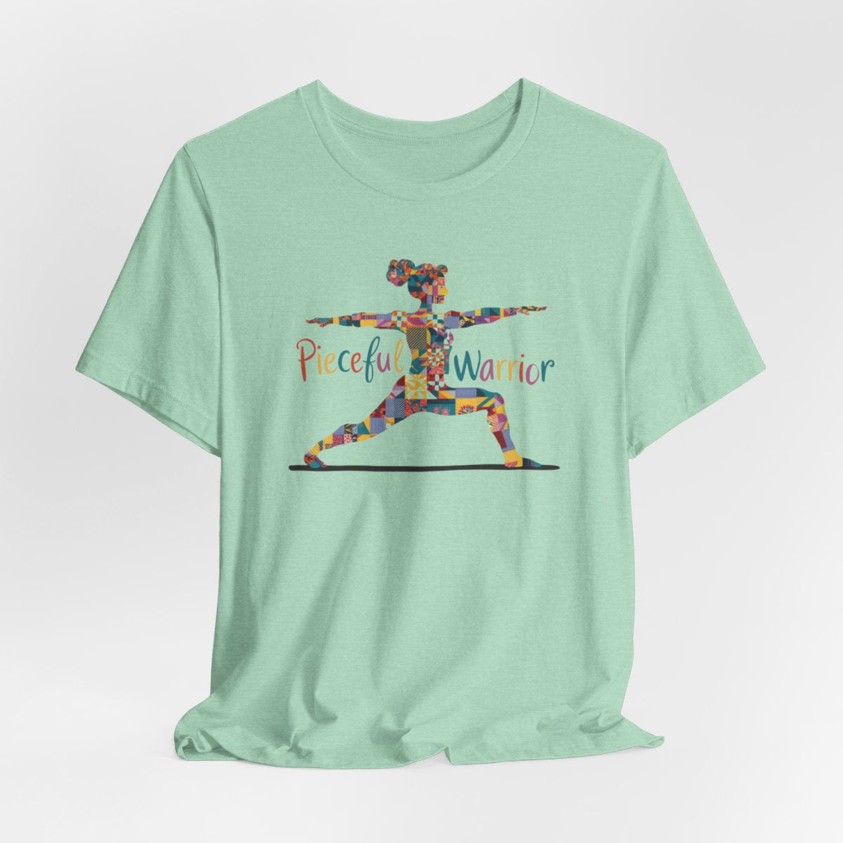 A Heather Mint Tee featuring a colorful patchwork silhouette of woman in yoga warrior pose. Text reads "Pieceful Warrior" in multicolored lettering.