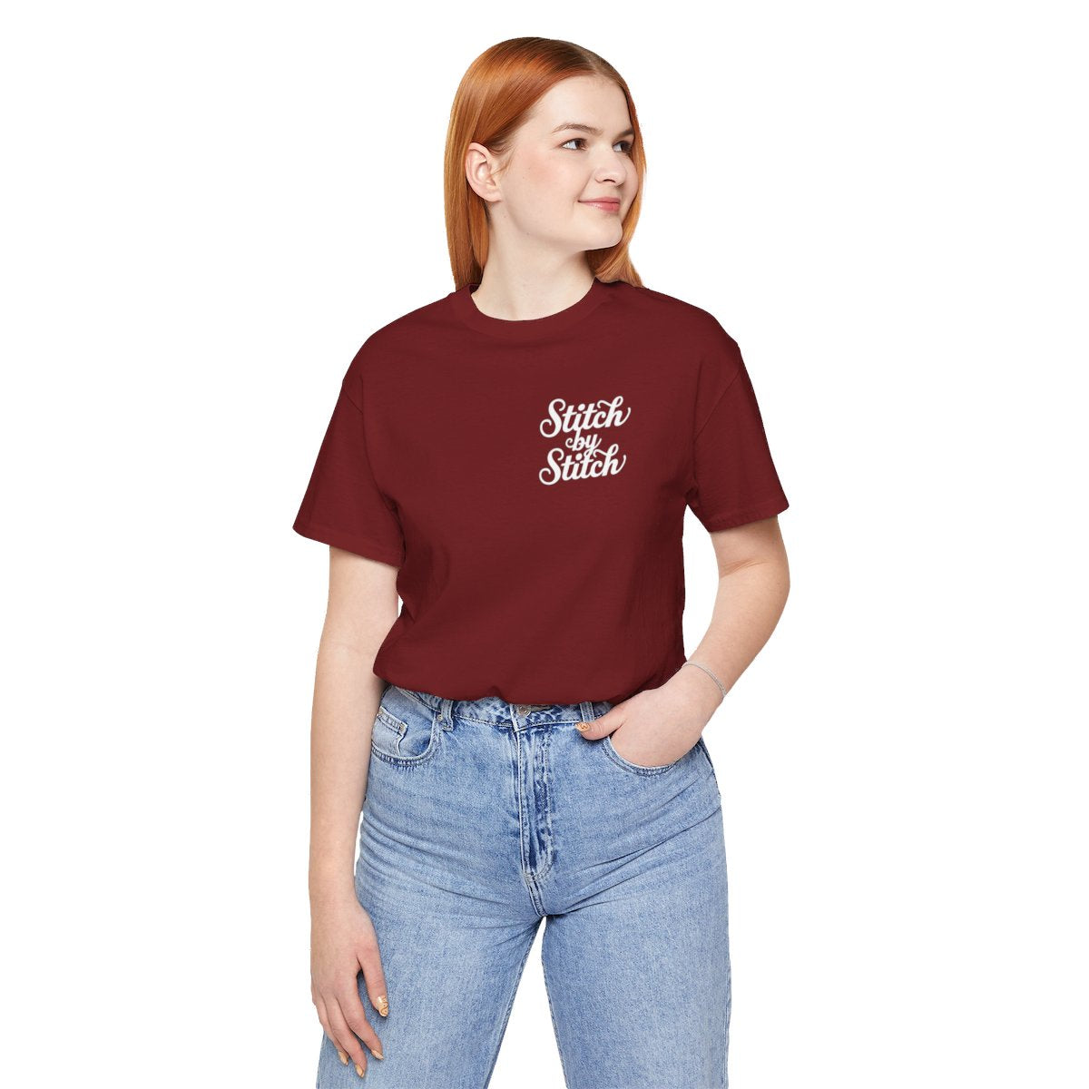 A Cardinal T-Shirt featuring the phrase "Stitch by Stitch". The word "Stitch" is written twice in a flowing script font, while "by" is centered between them in a smaller, sans-serif font. The design has a clean, minimalist aesthetic.