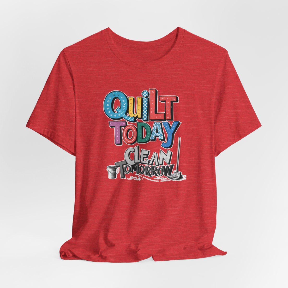 A Heather Red funny quilting T-Shirt with the phrase Quilt Today, Clean Tomorrow in a bold and cheerful font with a broom off to the side