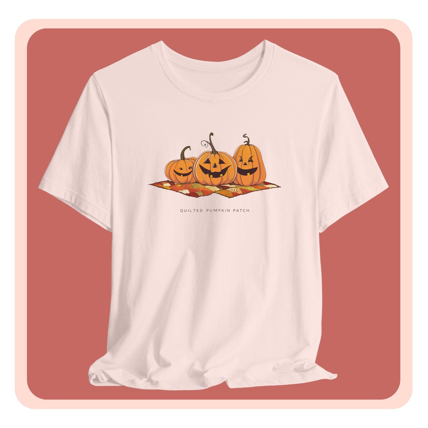 A T-shirt with three smiling jack-o'-lanterns sitting on a colorful autumn-themed quilt. The pumpkins have carved faces with various expressions, and the quilt beneath them features a patchwork of fall colors. Text below reads "QUILTED PUMPKIN PATCH".
