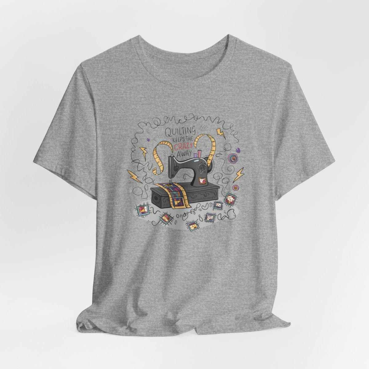 An Athletic Heather T-Shirt with a vintage sewing machine, measuring tape heart, and text "Quilting Keeps the Crazy Away" amidst swirls and quilting motifs.