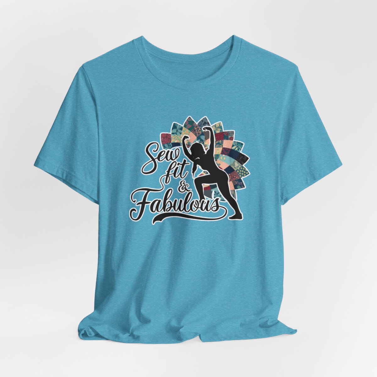A Heather Aqua T-Shirt featuring a black silhouette of woman with raised arms against colorful patchwork background. Text reads "Sew fit & Fabulous" in stylized script.