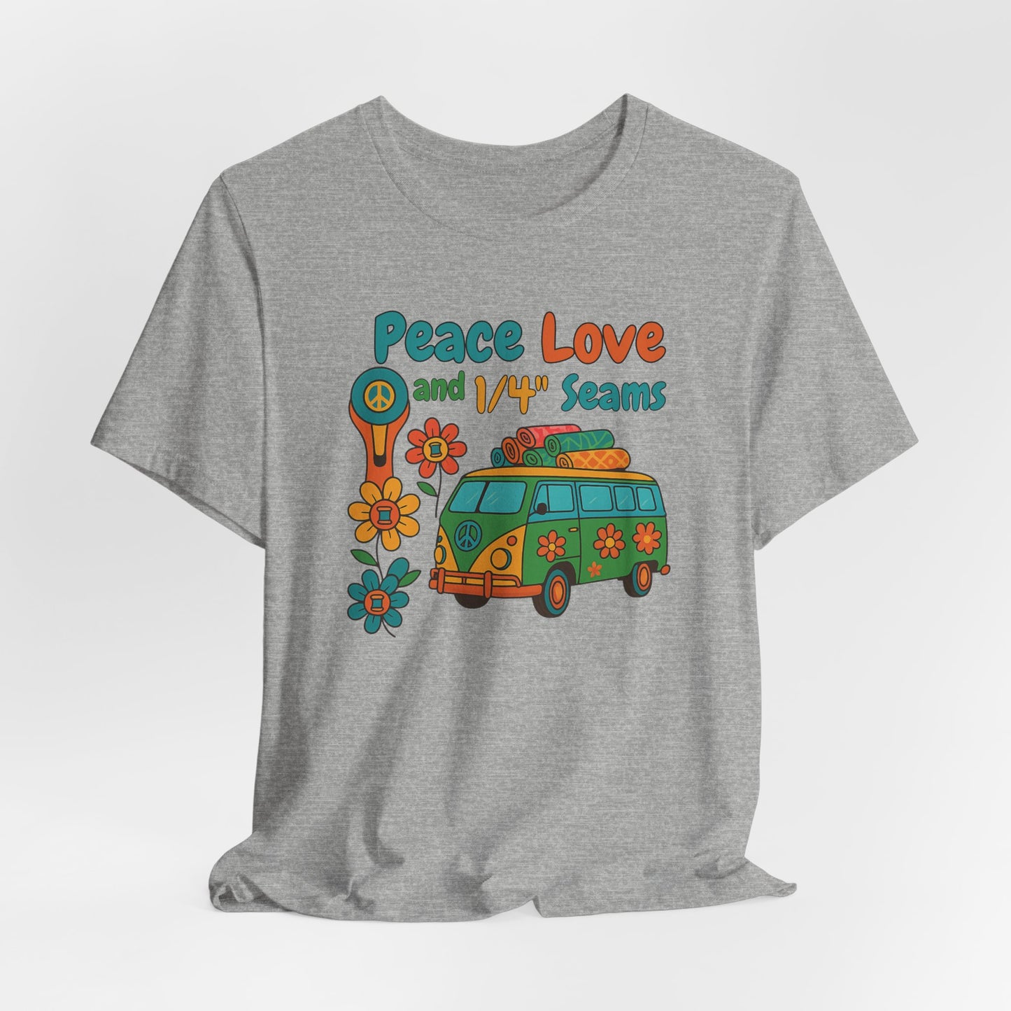 A An Athletic Heather t-shirt with colorful retro design showing a peace sign rotary cutter, patchwork van, and text “Peace Love and 1/4" Seams.” Surrounded by flowers made of thread spools. Fun vintage-style quilting shirt.
