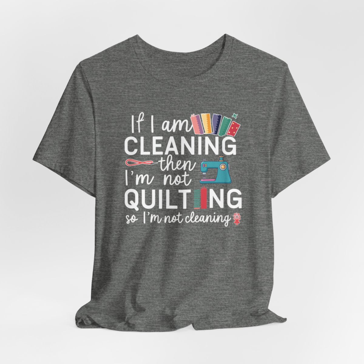 A Deep Heather funny quilting T-Shirt with the phrase If I am Cleaning then I'm not Quilting in a bold and cheerful font with images of quilting icons and supplies