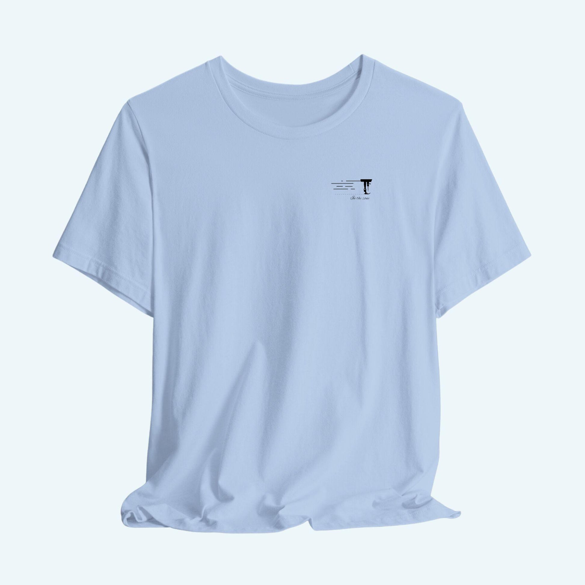 A T-shirt featuring a minimalist black silhouette of a sewing machine arm with motion lines. Below, the phrase "In the zone" is written in cursive script. The design conveys the focus and rhythm of quilting.
