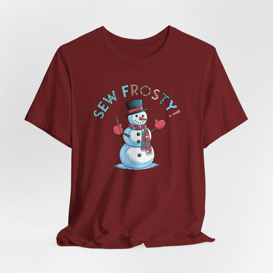 A Cardinal christmas quilting t-shirt featuring cheerful snowman design holding a sewing needle, with the phrase "Sew Frosty" in playful, winter-themed lettering. The snowman is wearing a scarf and mittens, ready for holiday sewing fun.