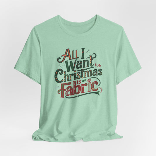 A Heather Mint festive quilting christmas T-shirt featuring the phrase "All I Want for Christmas is Fabric," with fun sewing and quilting accents like needles and threads swirling around the text.