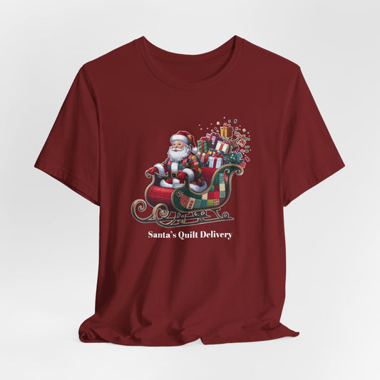 A Cardinal christmas quilting t-shirt featuring Santa Claus wearing a patchwork quilt coat, sitting in a sleigh filled with gifts and quilts, with the phrase "Santa's Quilt Delivery" below, combining holiday cheer and quilting fun.