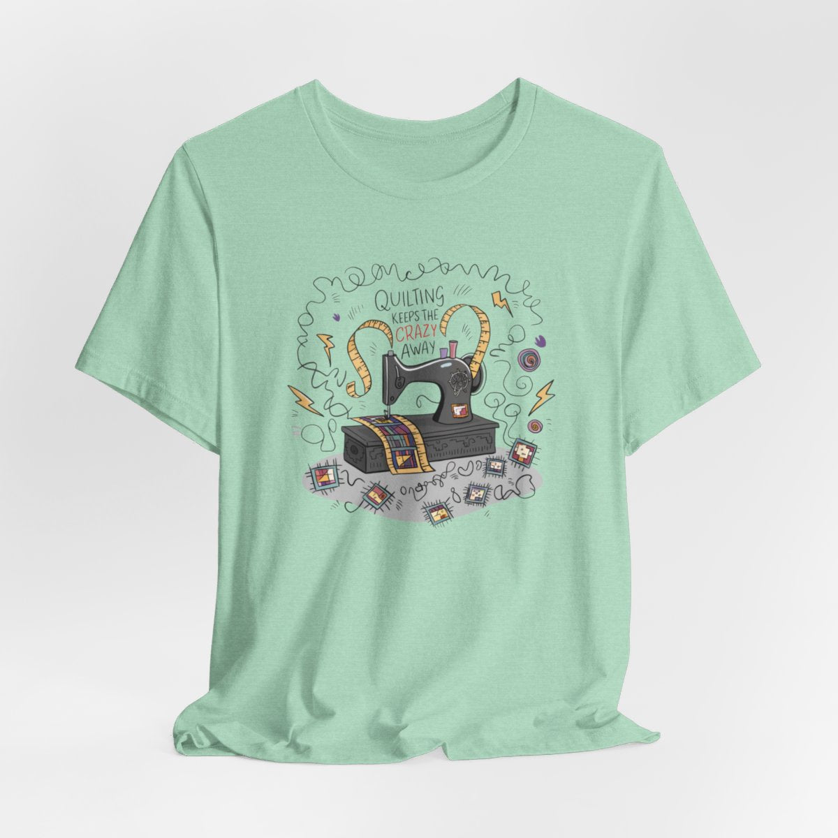A Heather Mint T-Shirt with a vintage sewing machine, measuring tape heart, and text "Quilting Keeps the Crazy Away" amidst swirls and quilting motifs.