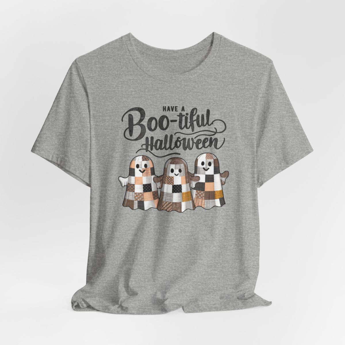 An Athletic Heather Halloween Quilting T-Shirt featuring three smiling patchwork ghosts made of various quilt patterns in autumn colors. Text reads "Have a Boo-tiful Halloween" in stylized lettering. Perfect for quilters who love Halloween.