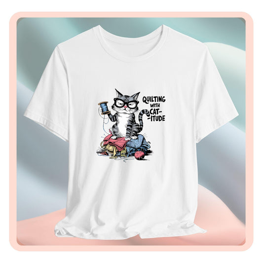 A t-shirt featuring a sassy cartoon cat sitting on a pile of colorful fabric, holding a spool of thread, with the phrase 'Quilting with Cat-itude,' perfect for quilters and cat lovers.