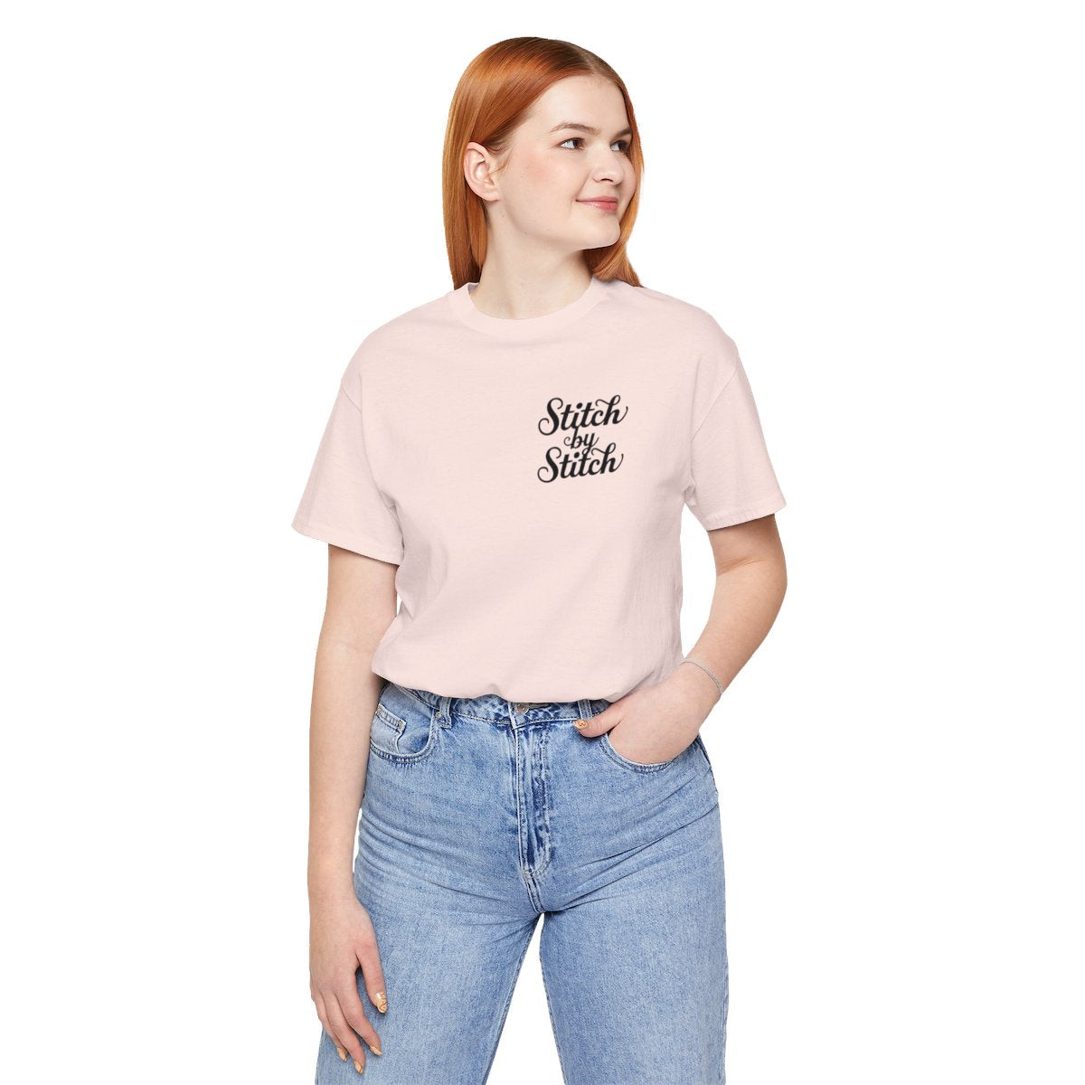 A Soft Pink T-Shirt featuring the phrase "Stitch by Stitch". The word "Stitch" is written twice in a flowing script font, while "by" is centered between them in a smaller, sans-serif font. The design has a clean, minimalist aesthetic.