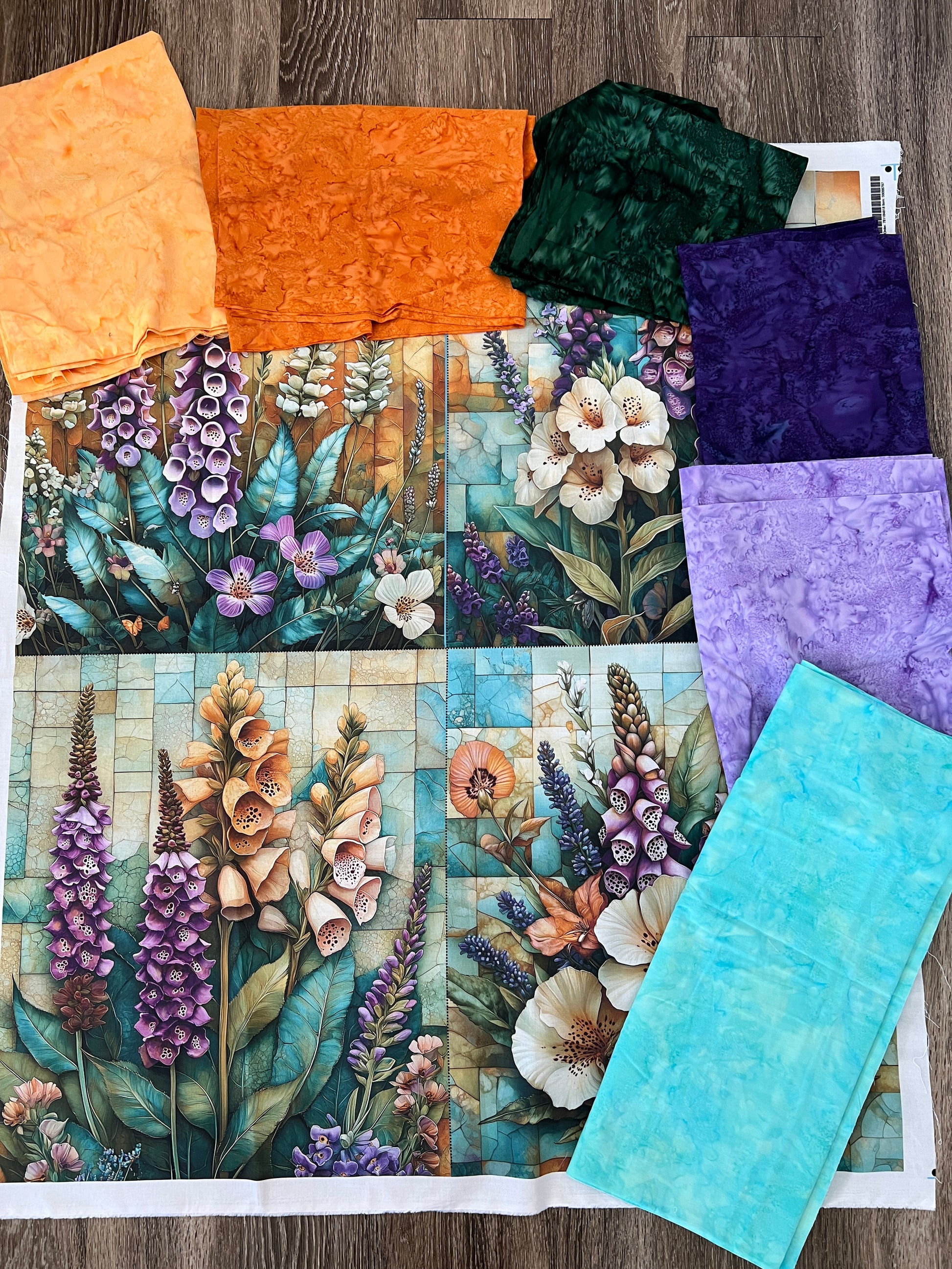 Foxglove and lavender quilt panel laid out with coordinating batik fabrics