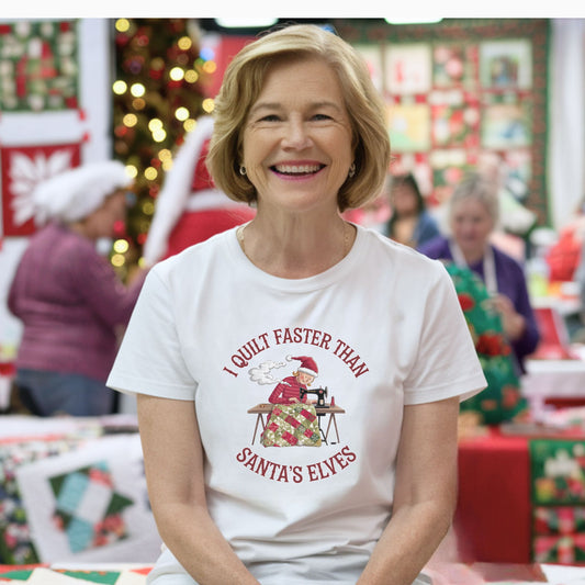 A christmas quilting t-shirt featuring  a quilter working at a sewing machine, quilting a festive holiday quilt, with the phrase "I Quilt Faster Than Santa's Elves" above the image, highlighting the speed and skill of the quilter.