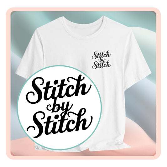 A T-Shirt featuring the phrase "Stitch by Stitch". The word "Stitch" is written twice in a flowing script font, while "by" is centered between them in a smaller, sans-serif font. The design has a clean, minimalist aesthetic.
