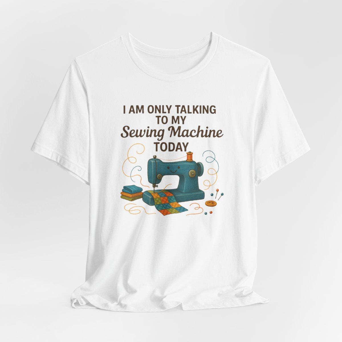 A White Short Sleeve T-Shirt featuring a smiling sewing machine with colorful fabric and playful thread swirls