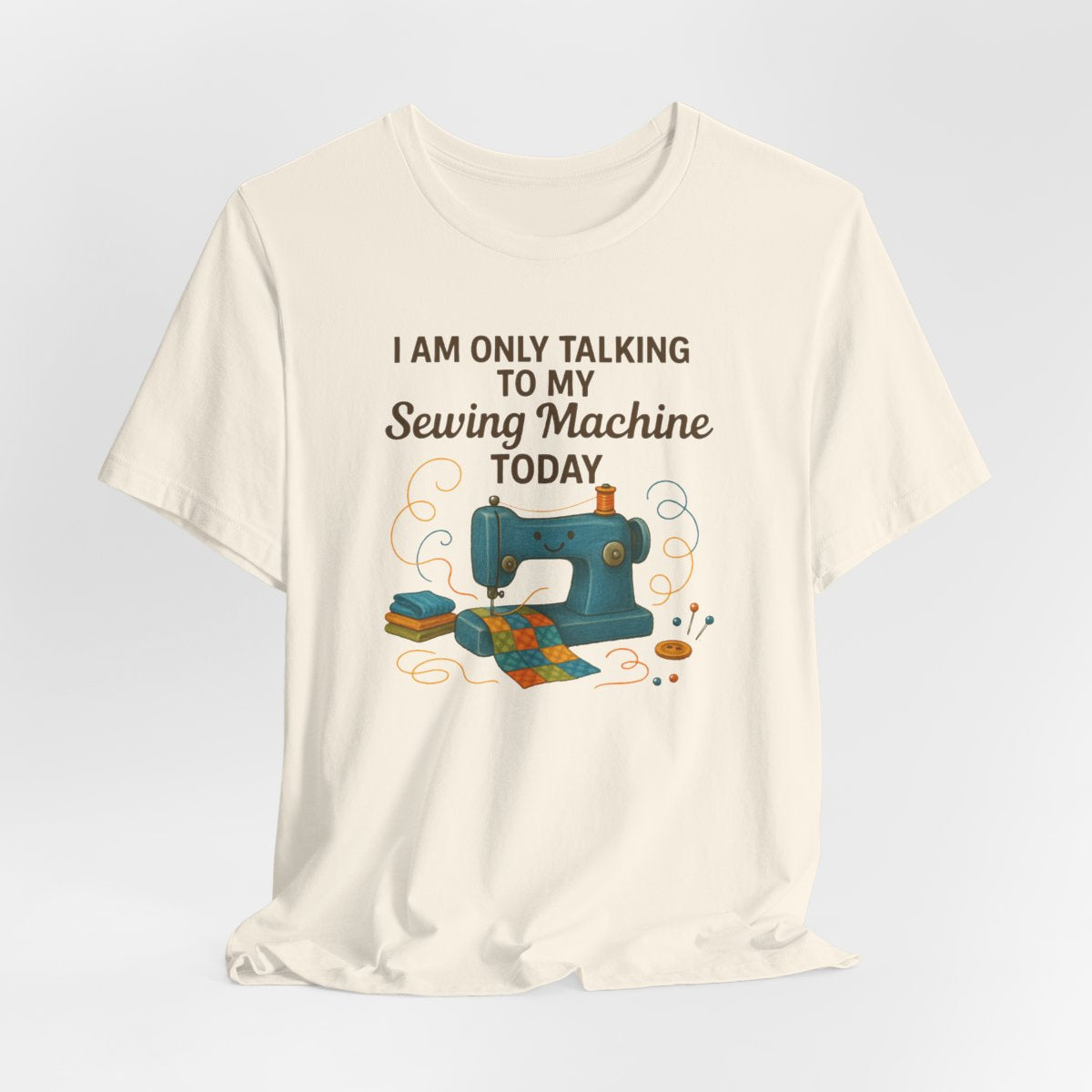 A Natural Short Sleeve T-Shirt featuring a smiling sewing machine with colorful fabric and playful thread swirls