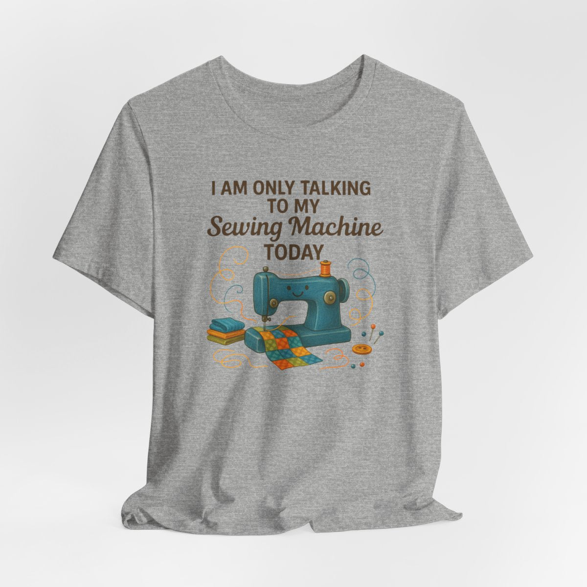 A Athletic Heather Short Sleeve T-Shirt featuring a smiling sewing machine with colorful fabric and playful thread swirls