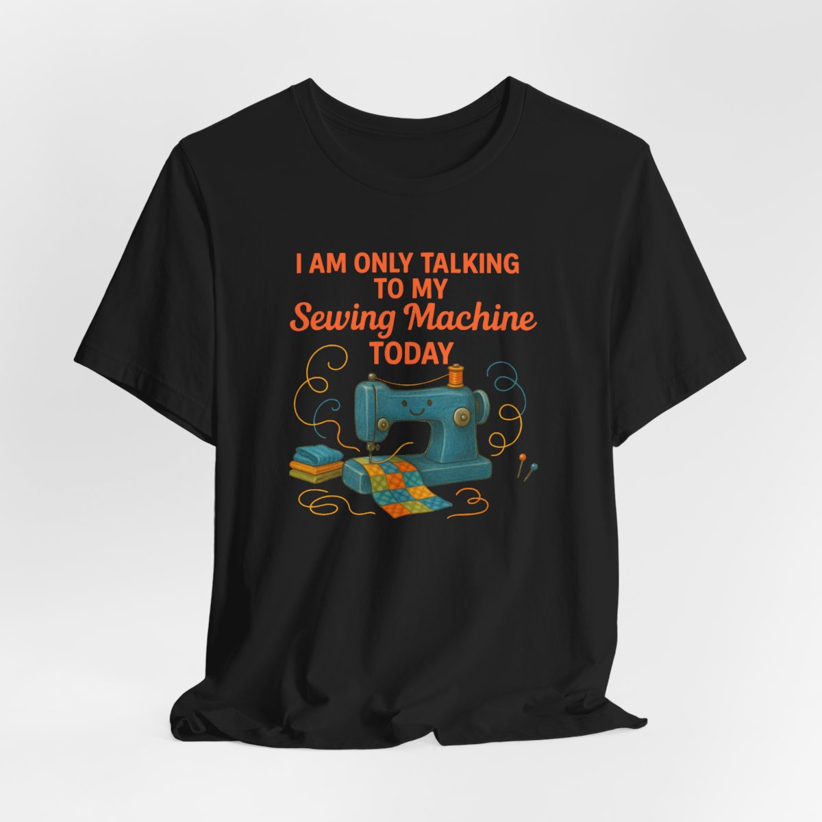 A Black Short Sleeve T-Shirt featuring a smiling sewing machine with colorful fabric and playful thread swirls