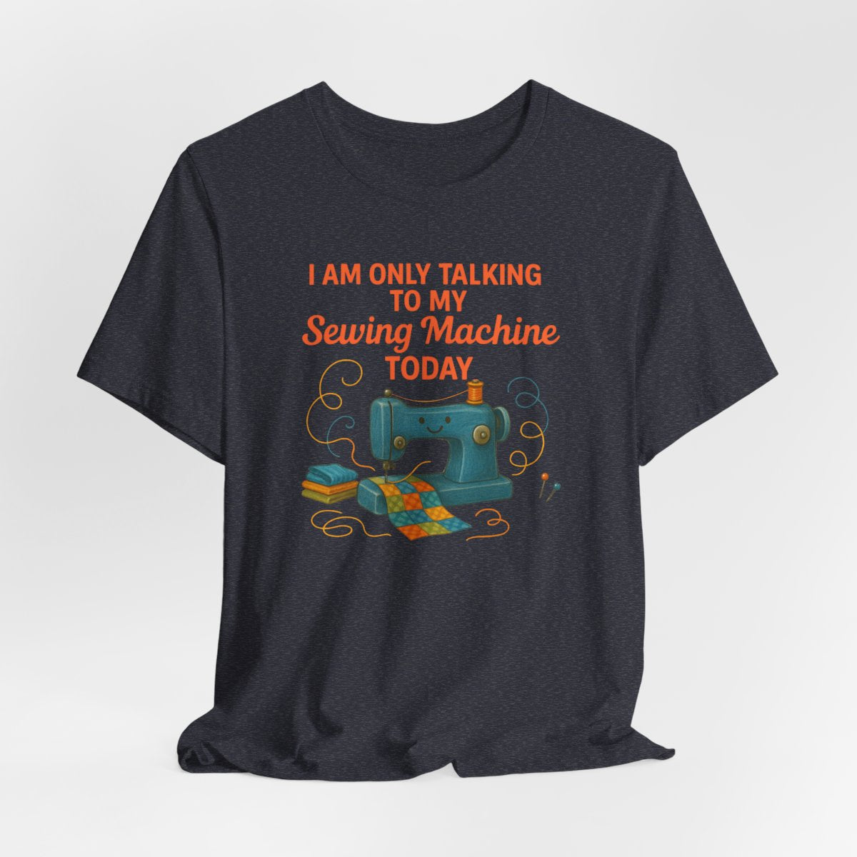 A Heather Navy Short Sleeve T-Shirt featuring a smiling sewing machine with colorful fabric and playful thread swirls
