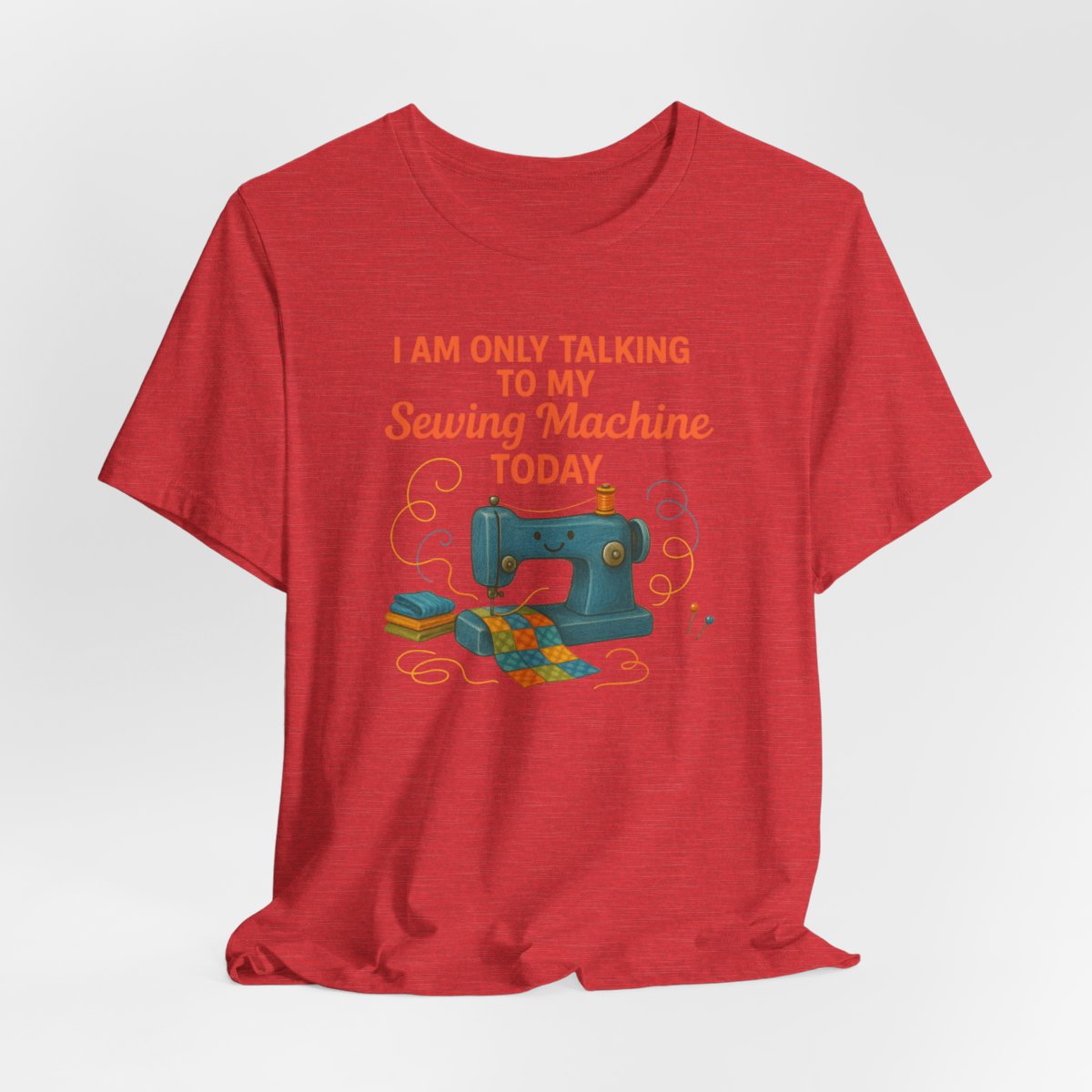 A Heather Red Short Sleeve T-Shirt featuring a smiling sewing machine with colorful fabric and playful thread swirls