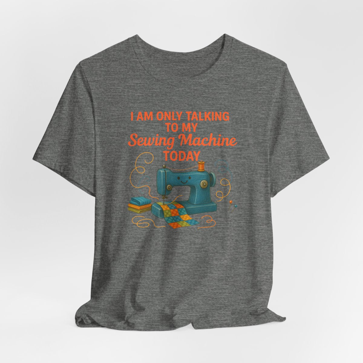 A Deep Heather Short Sleeve T-Shirt featuring a smiling sewing machine with colorful fabric and playful thread swirls