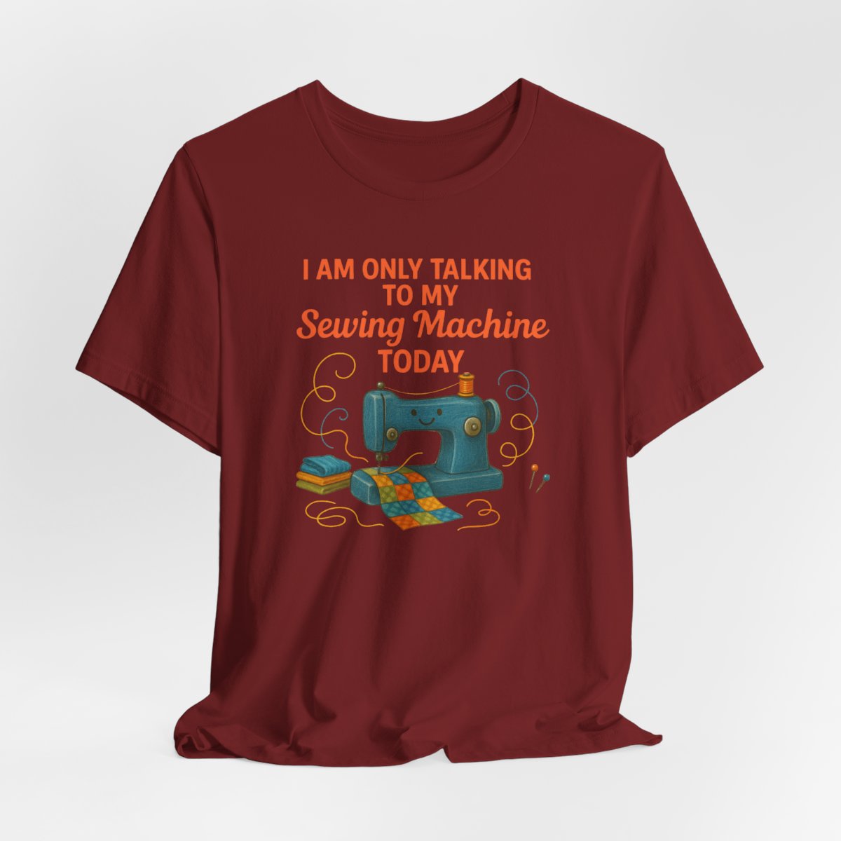 A Cardinal Short Sleeve T-Shirt featuring a smiling sewing machine with colorful fabric and playful thread swirls