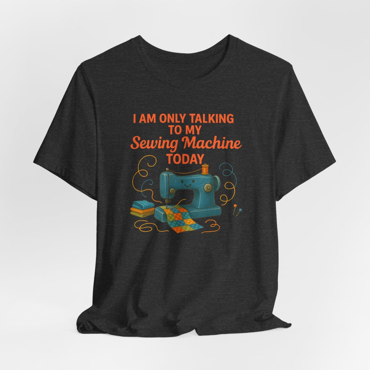 A Dark Grey Heather Short Sleeve T-Shirt featuring a smiling sewing machine with colorful fabric and playful thread swirls