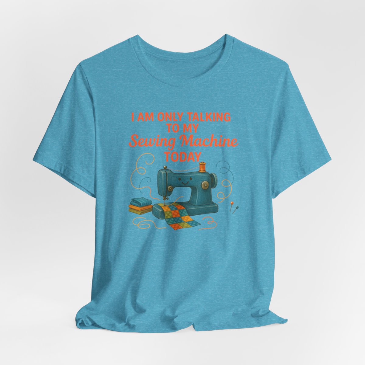 A Heather Aqua Short Sleeve T-Shirt featuring a smiling sewing machine with colorful fabric and playful thread swirls