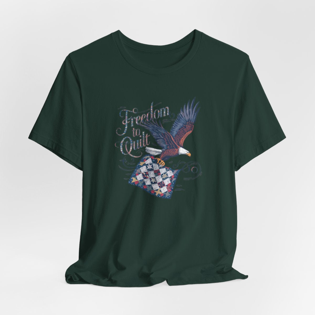 A Forest T-shirt with detailed illustration of a bald eagle in flight, carrying a patchwork quilt. Text reads "Freedom to Quilt" in an ornate, patriotic font.