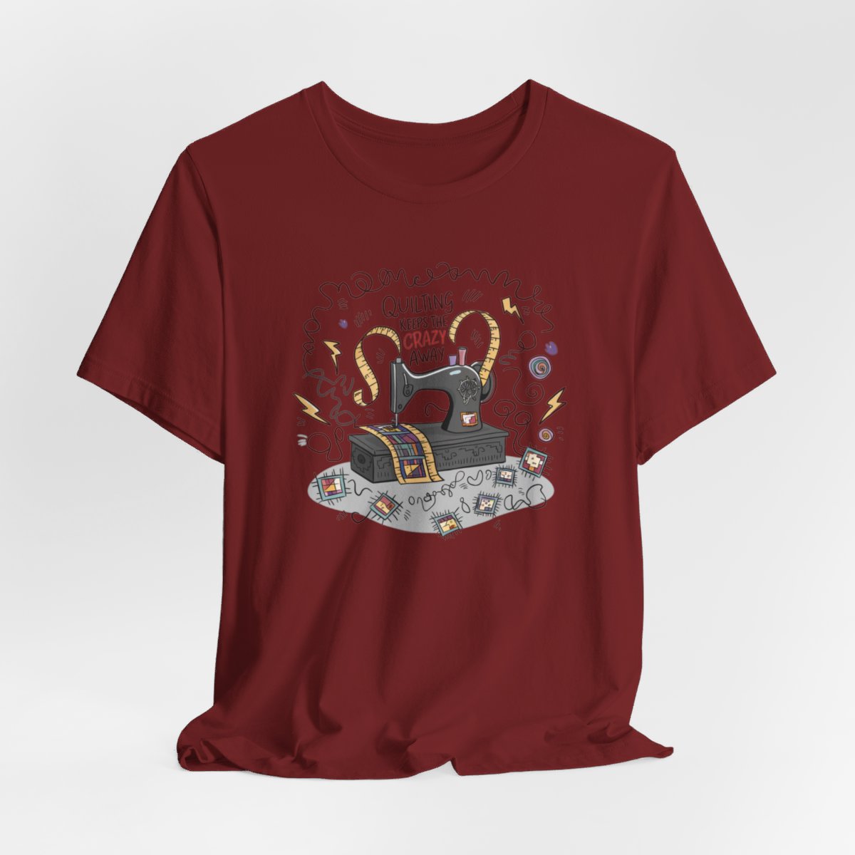 A Cardinal T-Shirt with a vintage sewing machine, measuring tape heart, and text "Quilting Keeps the Crazy Away" amidst swirls and quilting motifs.