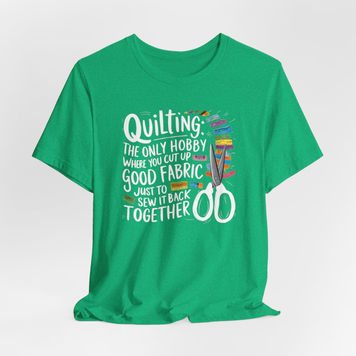 A Heather Kelly Quilting-themed T-Shirt with text "Quilting: The Only Hobby Where You Cut Up Good Fabric Just to Sew it Back Together" surrounded by colorful fabric scraps and scissors.