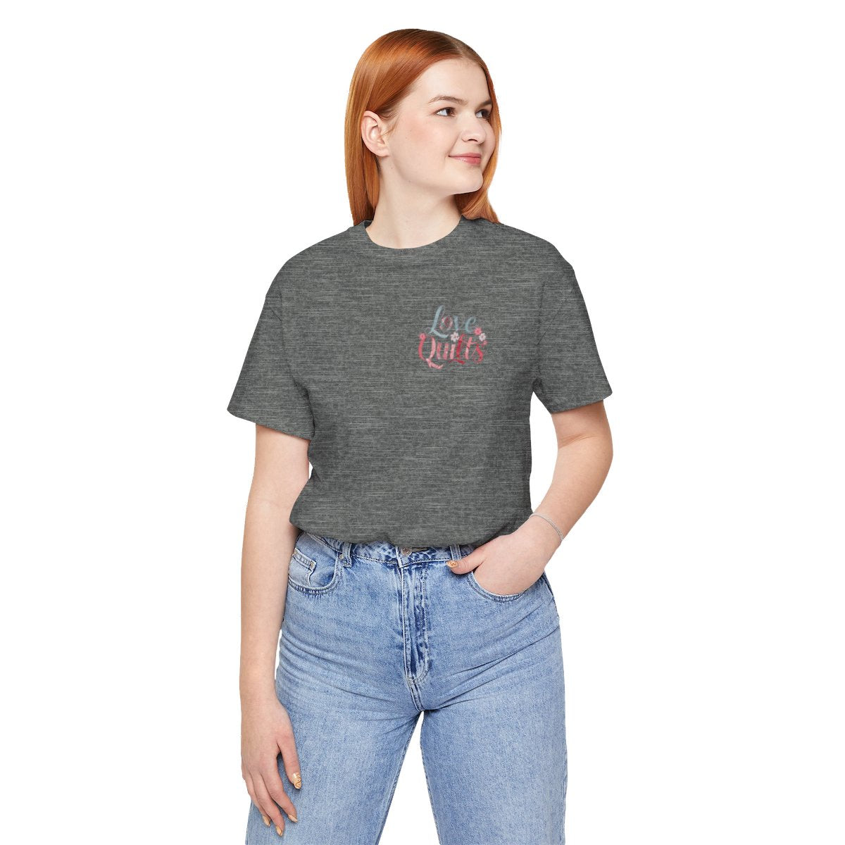 A Deep Heather t-shirt spelling out "Love Quilts". The word "Love" is in teal, while "Quilts" features various shades of pink and red. Small flowers in white and pink adorn the letters, creating a floral and quilting-inspired artwork.