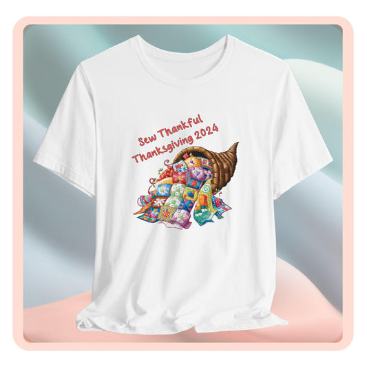 A thanksgiving  quilting t-shirt featuring a colorful quilted cornucopia overflowing with various quilt patterns and designs. Text reads "Sew Thankful Thanksgiving 2024" in red. Vibrant illustration combines quilting motifs with Thanksgiving imagery.