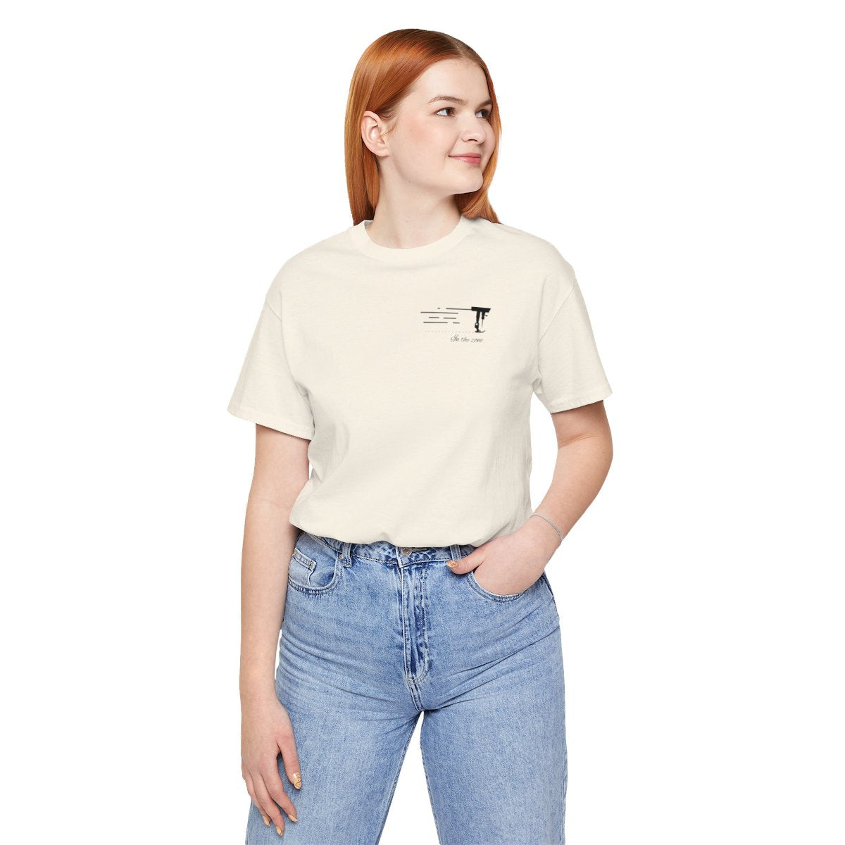 A Natural T-shirt featuring a minimalist black silhouette of a sewing machine arm with motion lines. Below, the phrase "In the zone" is written in cursive script. The design conveys the focus and rhythm of quilting.
