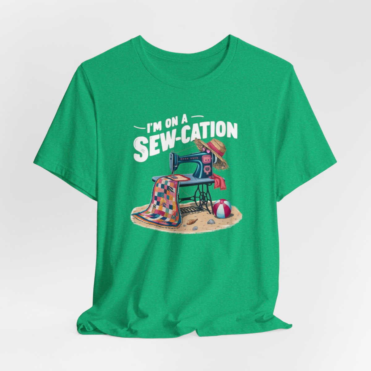 A Heather Kelly fun Quilting T-shirt of a vintage sewing machine on a beach with a colorful quilt, sun hat, and beach ball. Text above reads "I'm on a Sew-cation" in bold letters.