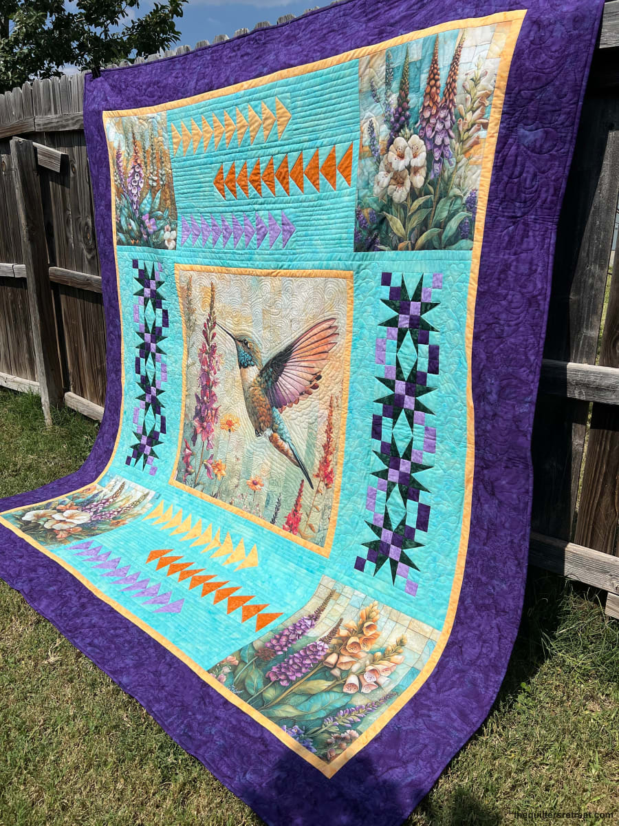 Foxglove blocks and hummingbird panel sewn into a purple quilt, draped outdoors