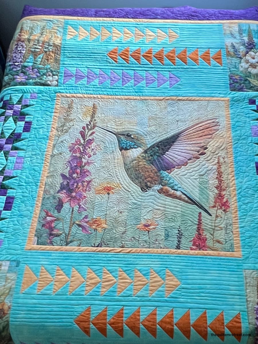 Close detail of the turquoise Hummingbird Garden quilt on a bed