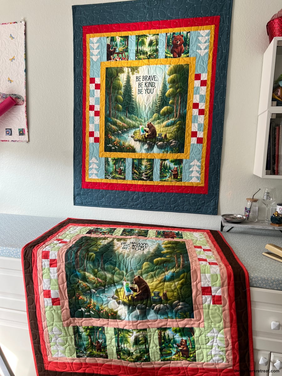 Two finished Be Kind Bear quilts — the bear-and-stream panel quilt kit shown in blue and green colorways