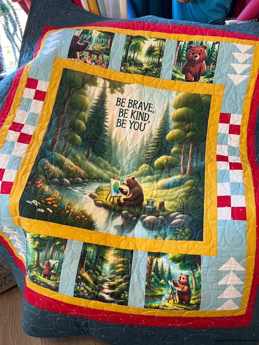 Finished Be Kind Bear panel quilt — forest bear scene with a red border and pieced bear blocks