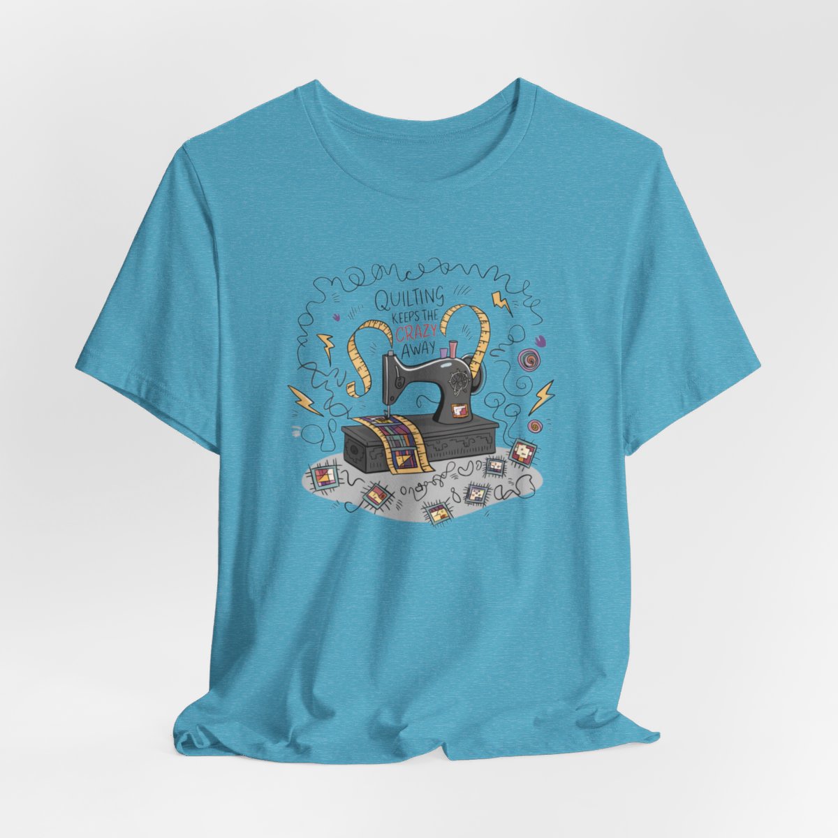 A Heather Aqua T-Shirt with a vintage sewing machine, measuring tape heart, and text "Quilting Keeps the Crazy Away" amidst swirls and quilting motifs.