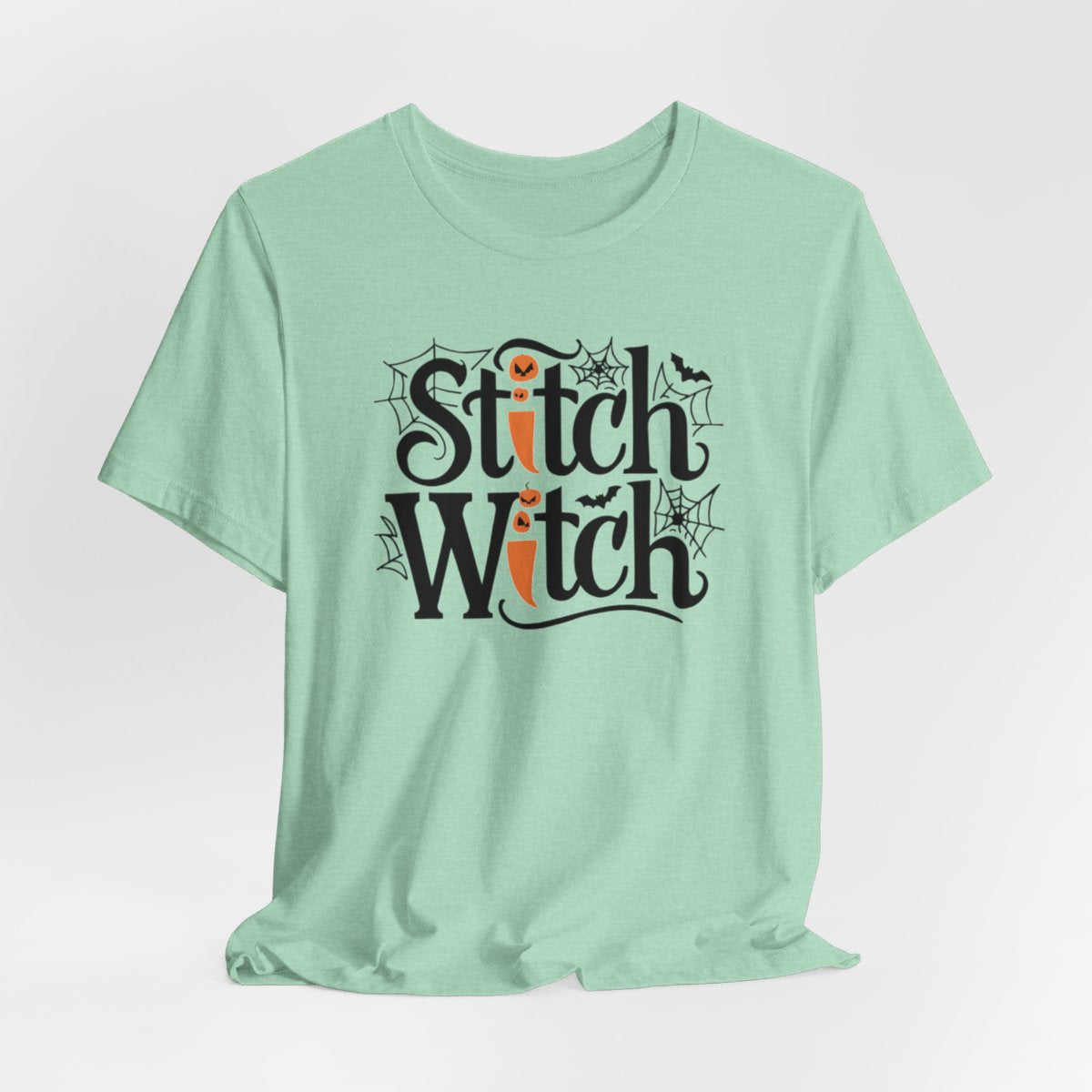 T-shirt design with "Stitch Witch" text in Halloween-themed typography. Jack-o'-lanterns, spiderwebs, and bats decorate the letters. The "i" in "Stitch" resembles a sewing needle. Ideal for quilters who love Halloween.