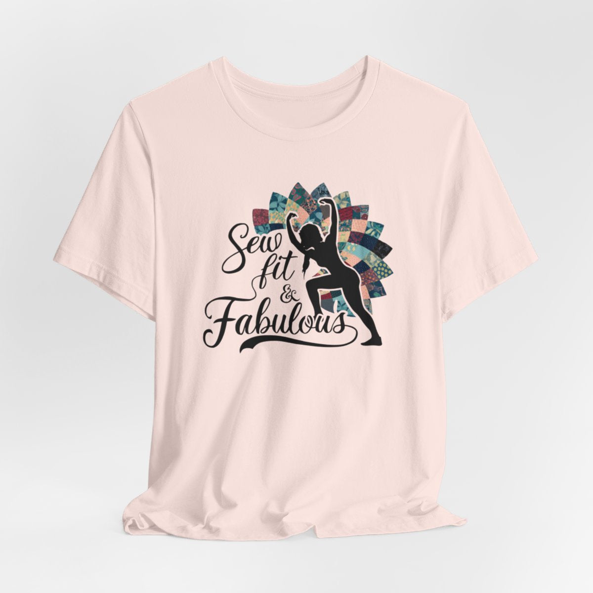 A Soft Pink T-Shirt featuring a black silhouette of woman with raised arms against colorful patchwork background. Text reads "Sew fit & Fabulous" in stylized script.
