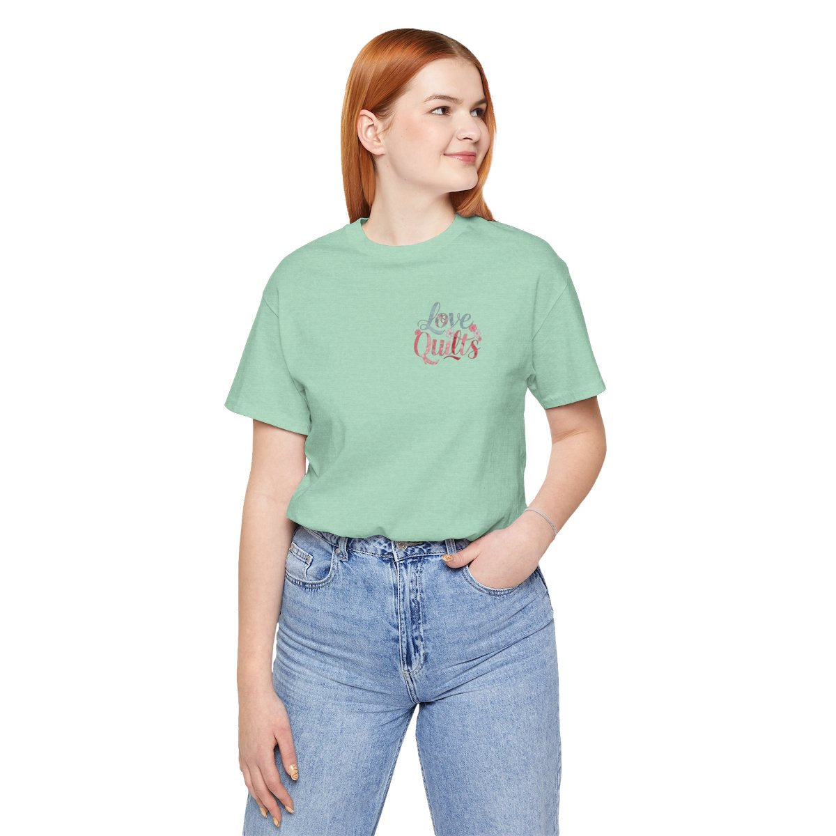 A Heather Mint t-shirt spelling out "Love Quilts". The word "Love" is in teal, while "Quilts" features various shades of pink and red. Small flowers in white and pink adorn the letters, creating a floral and quilting-inspired artwork.