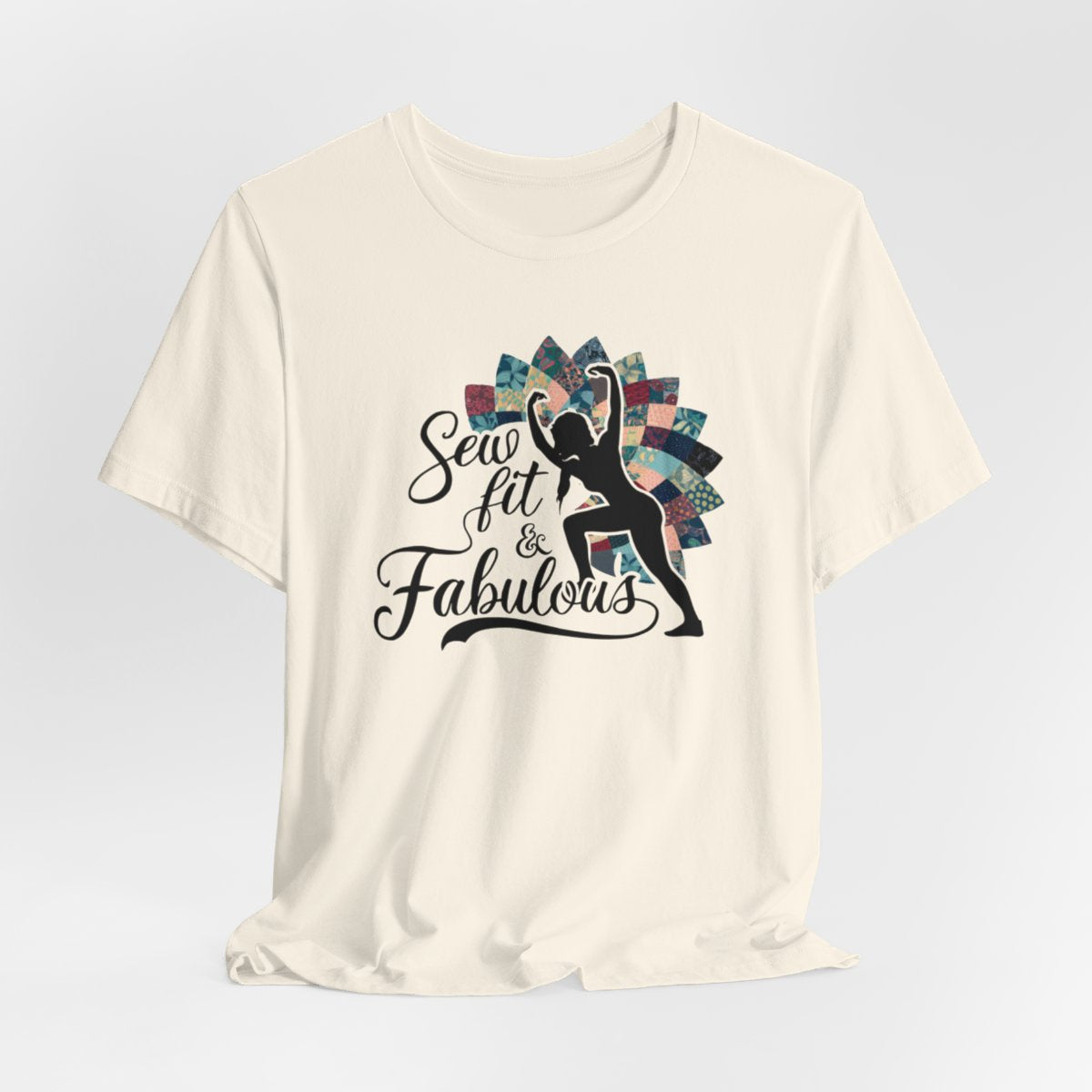 A Natural T-Shirt featuring a black silhouette of woman with raised arms against colorful patchwork background. Text reads "Sew fit & Fabulous" in stylized script.