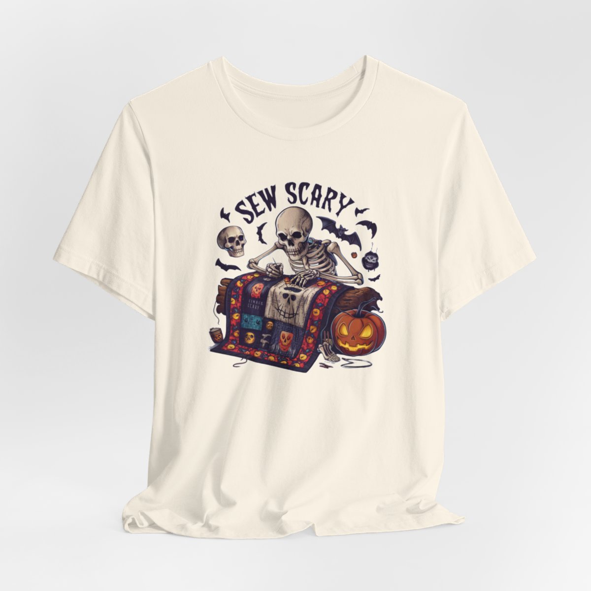 A Natural Halloween Quilting T-Shirt featuring a skeleton sewing Halloween quilt. Colorful patchwork with spooky motifs. Bats and pumpkins surround skeleton. Text reads "Sew Scary". Ideal for quilters who love Halloween.